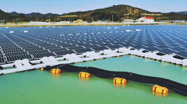 Foto de uma superfície grande de água com diversos painéis fotovoltaicos instalados em estruturas brancas parecidas com plástico. Ao fundo, uma colina coberta por vegetação. Usina flutuante da Kyocera.