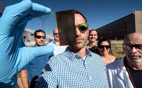 homem segura uma pequena placa de vidro metade transparente, metade colorida de um tom marrom escuro. É a nova janela solar desenvolvida nos EUA